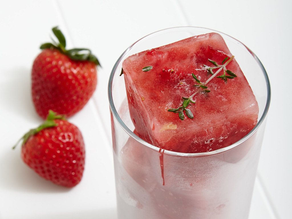 strawberry and thyme ice cubes in a glass next to strawberries