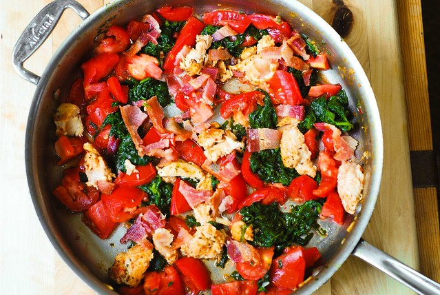 combining vegetables, tomatoes, spinach, bacon, and chicken for pasta dinner recipe