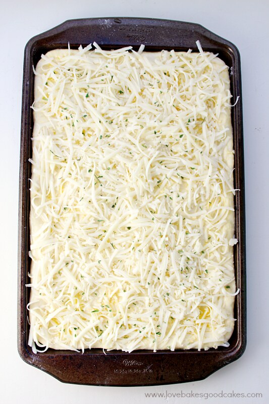 Cheesy Breadsticks dough in the baking pan sprinkled with mozzarella cheese and chopped parsley.