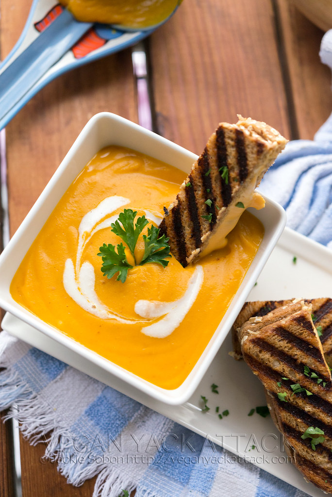Square white bowl with bright orange butternut bisque inside, with grilled cheese stick dipped inside