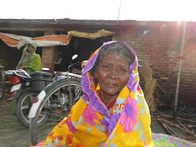 Kamrun Khatoon, and elderly woman sitting and pondering outside of her burnt house in village Azizpur.
