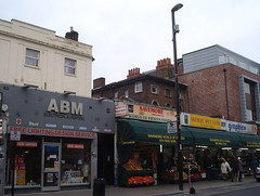 Four shopfronts along the ground floor of a terrace.  Two older buildings and one modern one are visible rising above these ground-floor extensions.