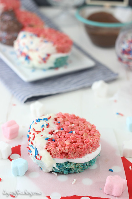 Celebrate with these Patriotic Rice Krispie Treat S'mores. Red and blue Rice Krispie Treats smothered in marshmallow frosting and dipped in chocolate.