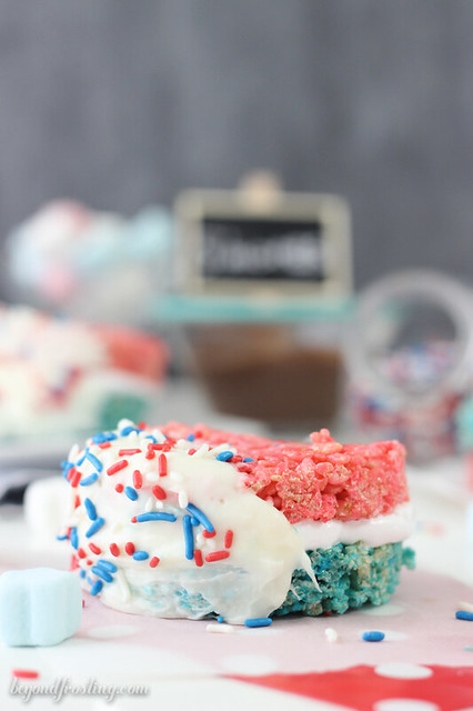 Celebrate with these Patriotic Rice Krispie Treat S'mores. Red and blue Rice Krispie Treats smothered in marshmallow frosting and dipped in chocolate. 